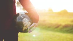 person holding black and brown globe ball while standing on grass land golden hour photography